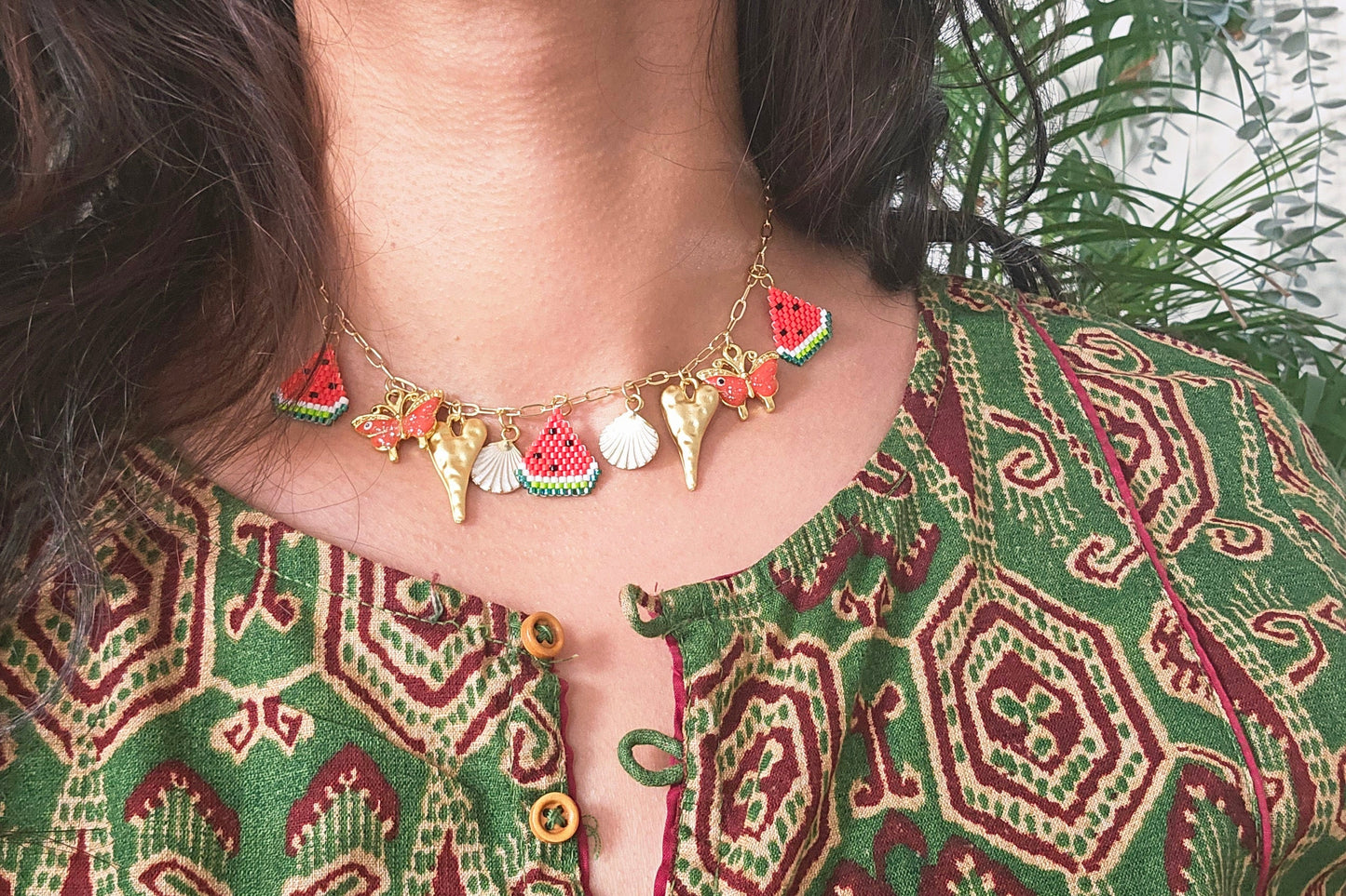 Woman wearing a green patterned top with a necklace and earrings, surrounded by plants.